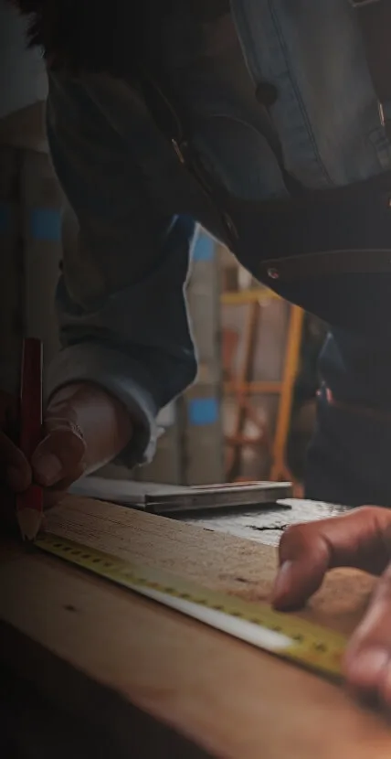 Handwerker misst Holzbrett und markiert Maße mit Bleistift