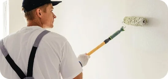 Maler streicht Innenwand mit Farbrolle gleichmäßig weiß