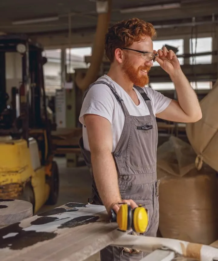 Handwerker in Werkstatt mit Schutzbrille und Gehörschutz bei Holzarbeiten